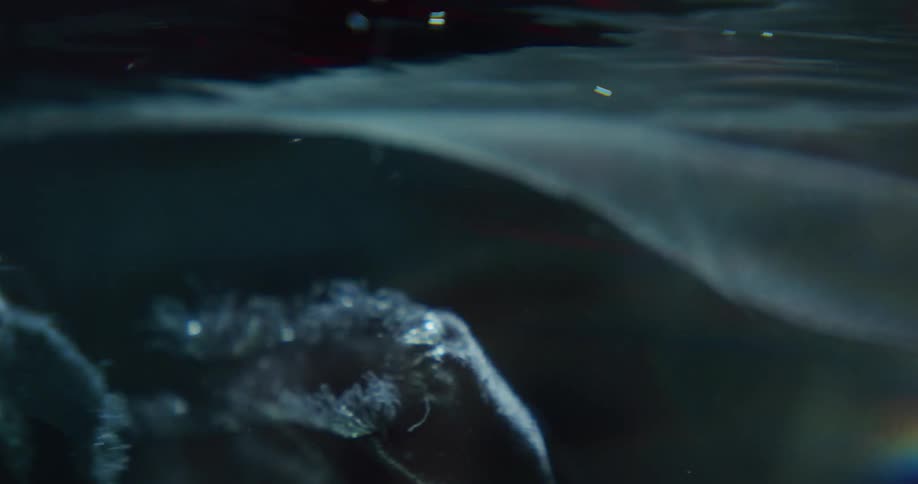 A blue cloth is moving underwater as light shines on the ripples and air bubbles rise