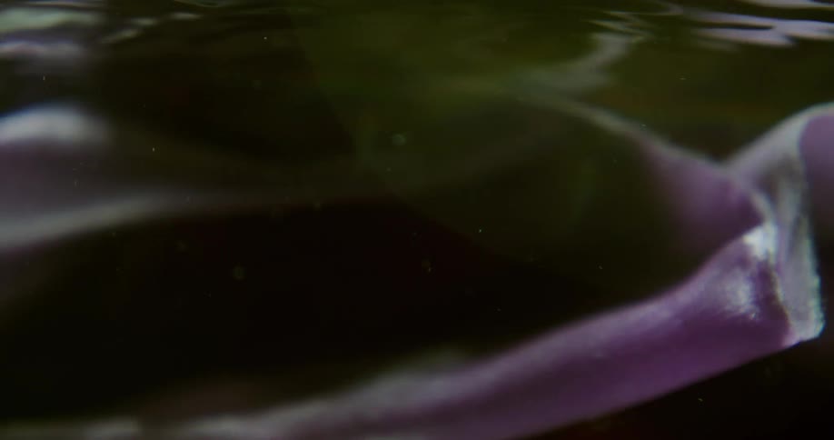 Underwater lavender colored fabric with flowing movement like washing machine with red light reflecting from above