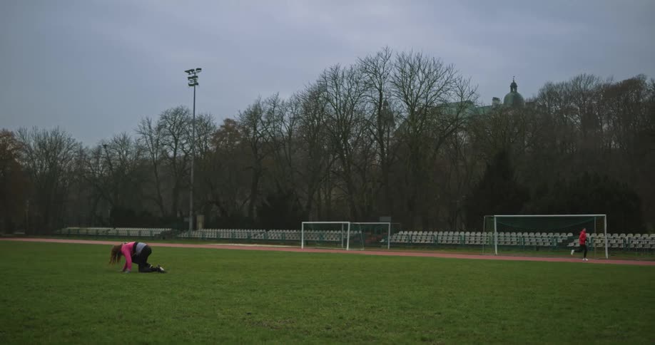 A woman limps across the grass in a stadium and falls down
