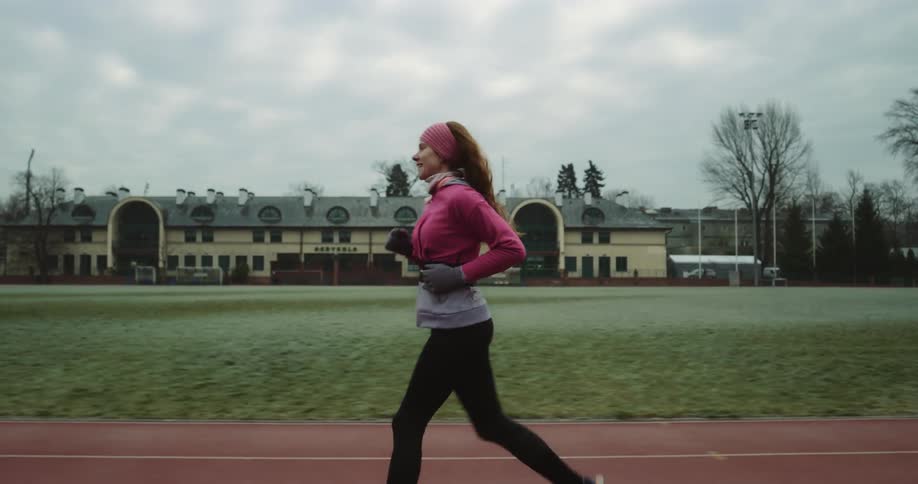 Woman jogs along track with large building in the distance