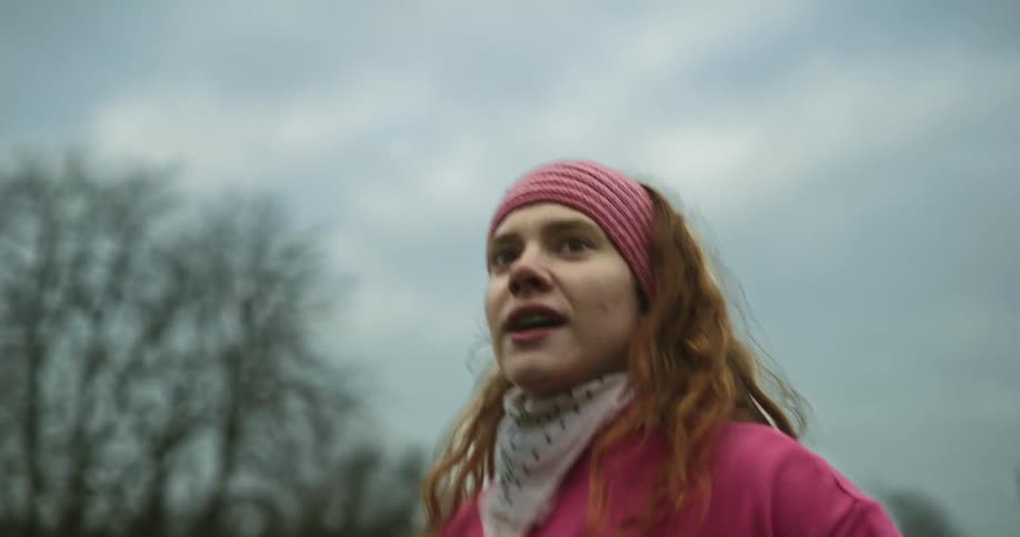 Woman with brown hair pink headband top and bandanna warms up and runs off on green lawn