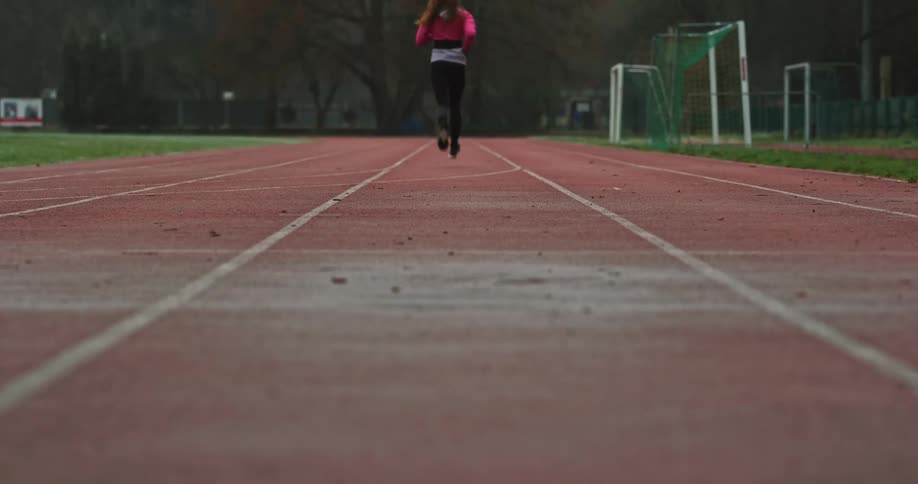 Woman with pink top black leggings and shoes runs on running track