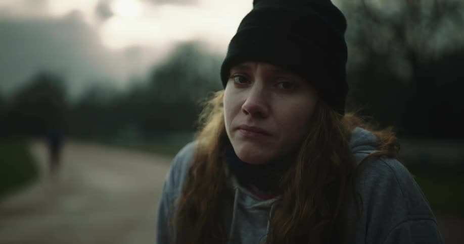 A woman slightly grimaces while looking at the camera as shes outdoors near a running track