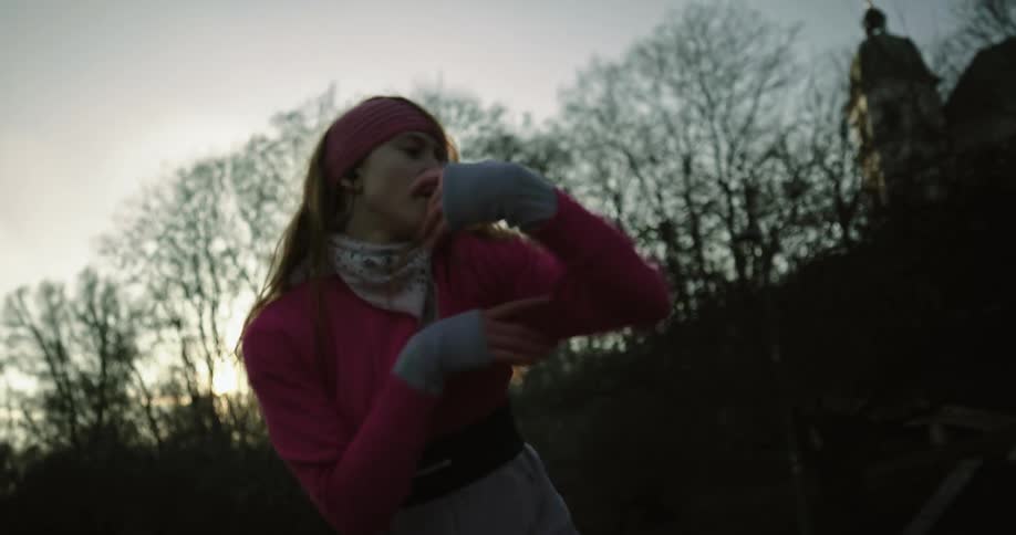 A woman flails her arms while dancing around a park