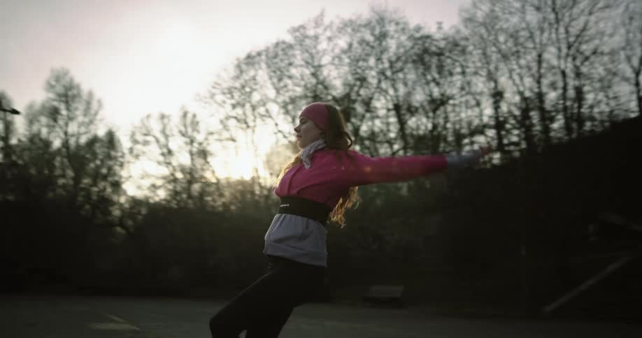 Woman dances near steps in area overlooked by large house on a hill
