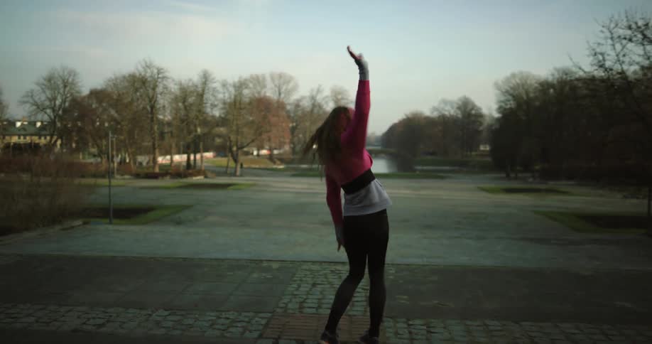 A woman is dancing outdoors in an empty parking lot