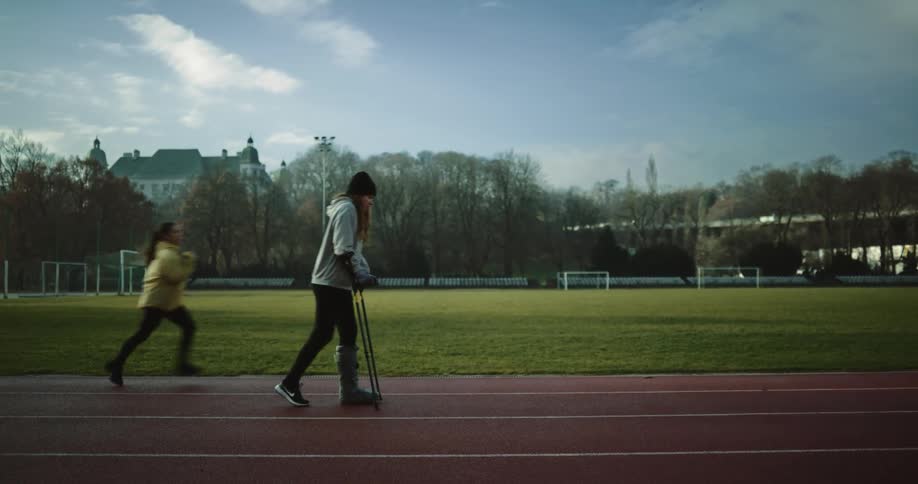 Woman on crutches speeds up while walking on running track as another woman runs past