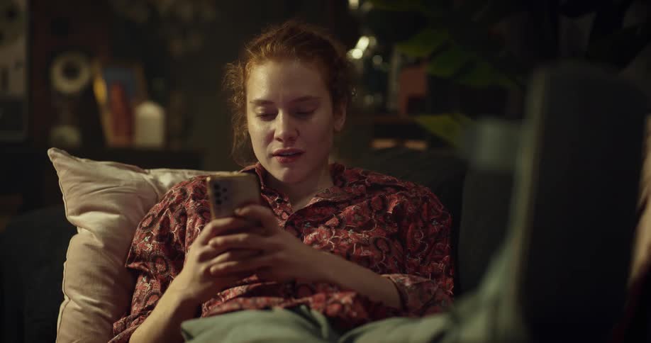 Woman smiles while using smartphone before putting it down an leaning back on couch with a smile