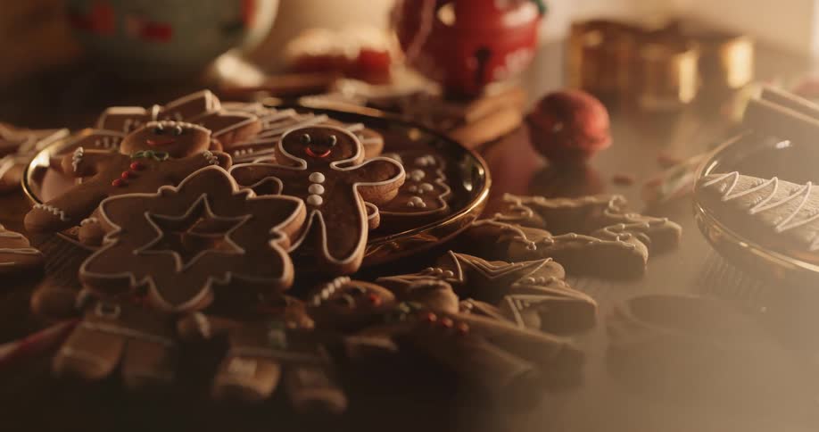 Iced gingerbread cookies spill from dish onto table near christmas ornaments