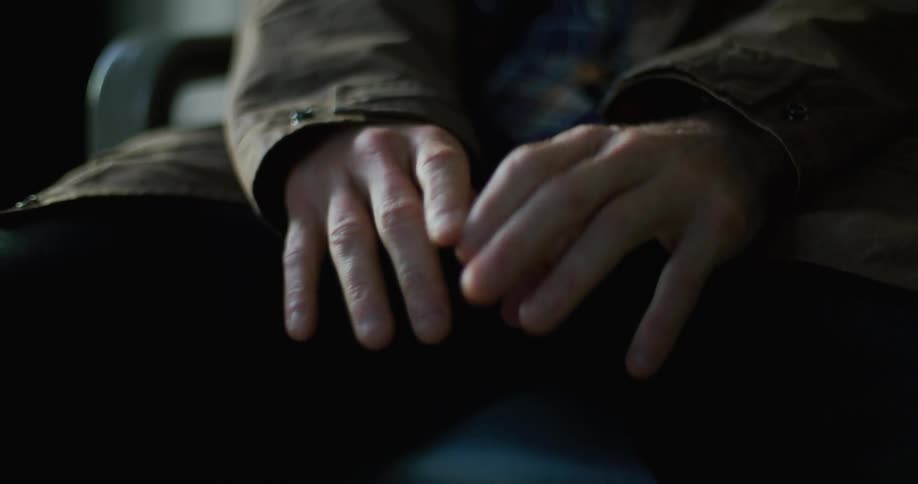 Sitting person clasps their trembling hand with their other hand to keep it still