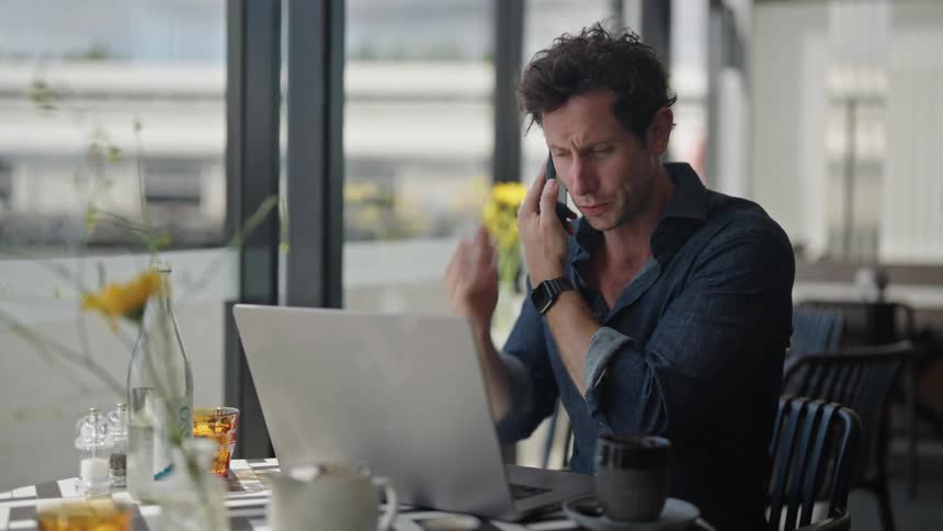 A man talking on phone with a client and also pressing his laptop which is on the table