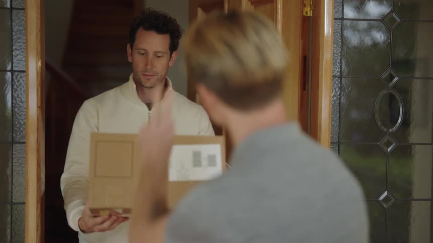 A man is standing at his front door as a delivery man hands him his package