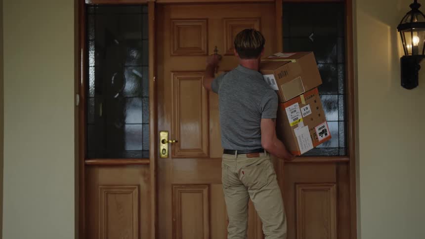 Blonde delivery man with gray top and brown pants delivers packages knocking door