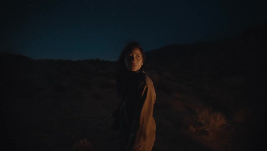A woman looks around a canyon at night and stops to take a photo