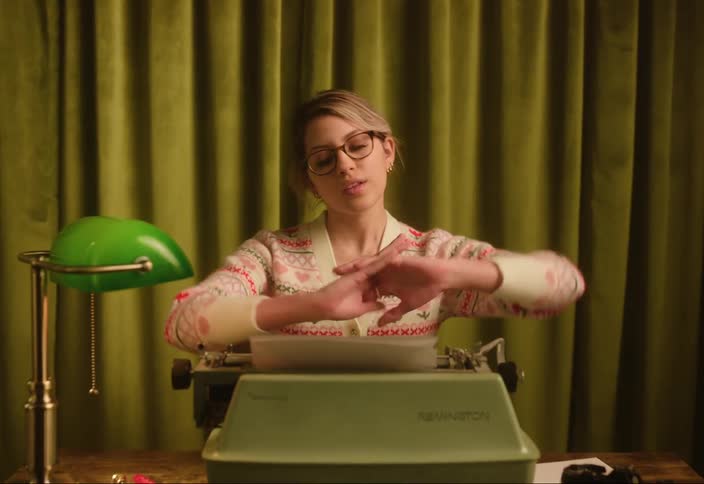 A woman slides her office chair to her desk and cracks her knuckles before typing on a typewriter