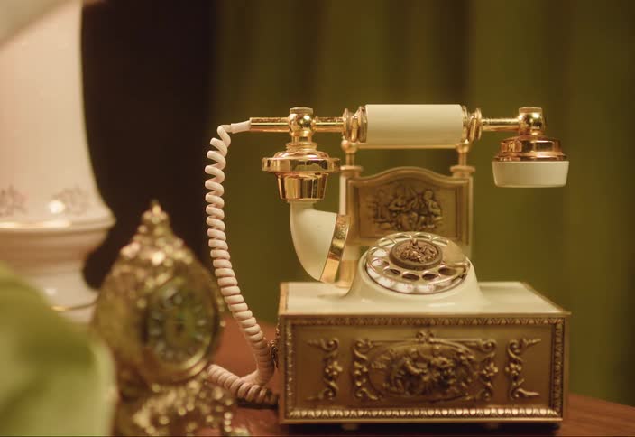 Woman wearing sweater hangs up gold decorated rotary telephone