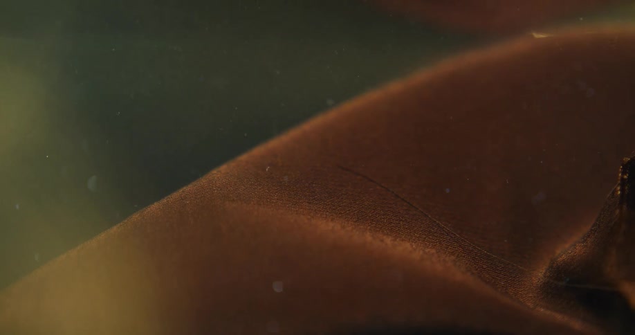 A peach colored cloth moves as it floats underwater as small bubbles rise