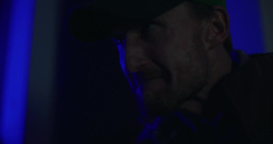 Man standing near wall grimaces as red and blue lights flash in the darkness