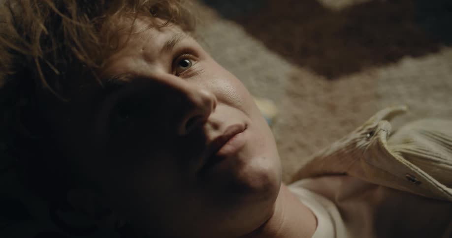 A young man is laying on a carpeted floor while reading a book in the daytime