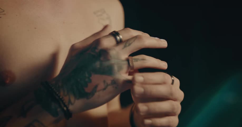 Bare chested man with tattoo on his arm and hand plays with his rings