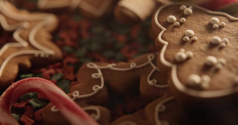 Holiday gingerbread cookies are decorated with icing as they sit on a table with candy canes