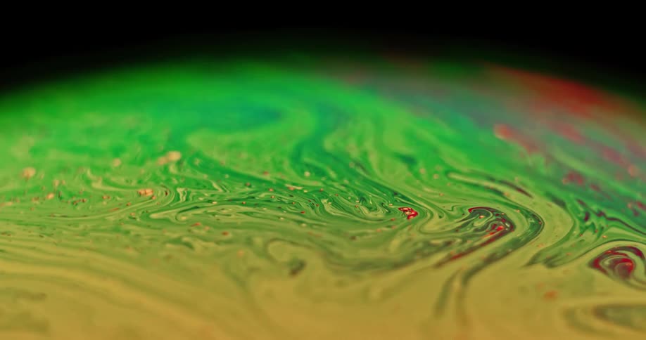 The organic green and yellow colored surface of a sphere blends as it turns with red speckles mixing in