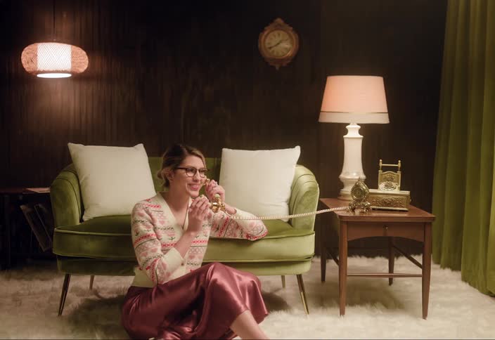 A woman is sitting down and talking on a telephone