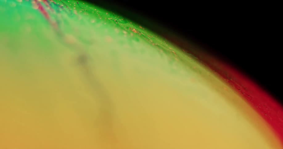 The surface of an orb turns as green blends with yellow and yellow particles move over the green as red moves along the edge
