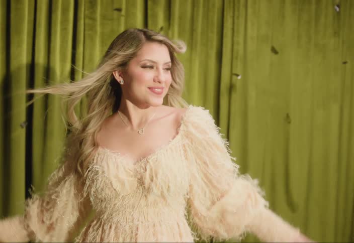 A woman with long blond hair smiles as she dances on stage with her arms up as confetti flies in the air