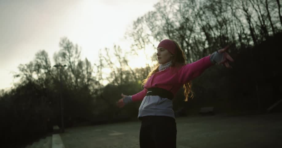A woman is dancing outdoors while the sun is setting