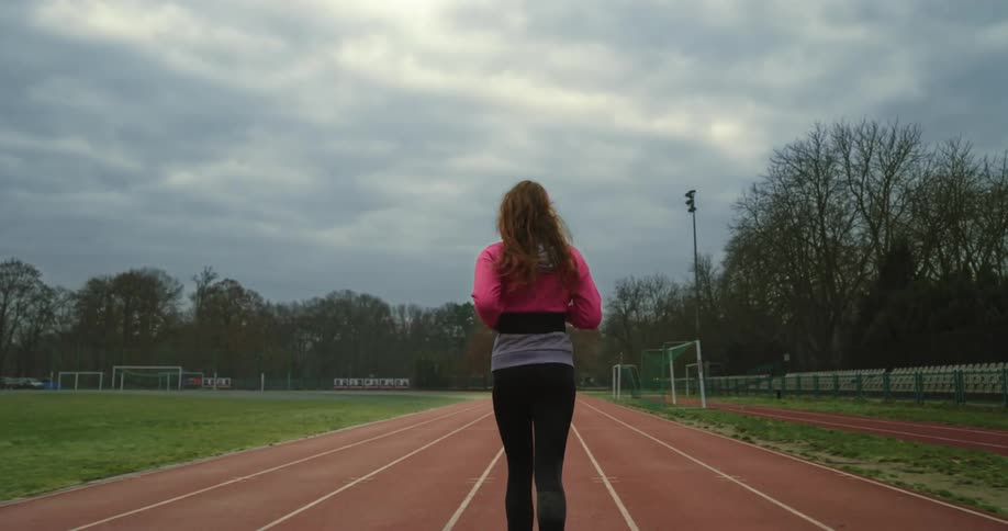 Woman with brown hair pink jacket and black leggings runs on running tracks