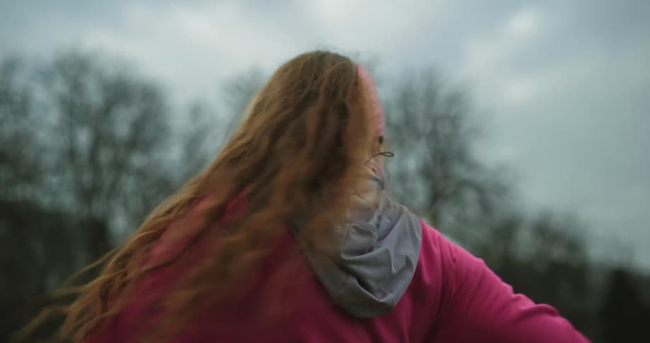 A woman outside and dressed in pink seems to be stretching by having her arms bent at her sides and twisting back and forth