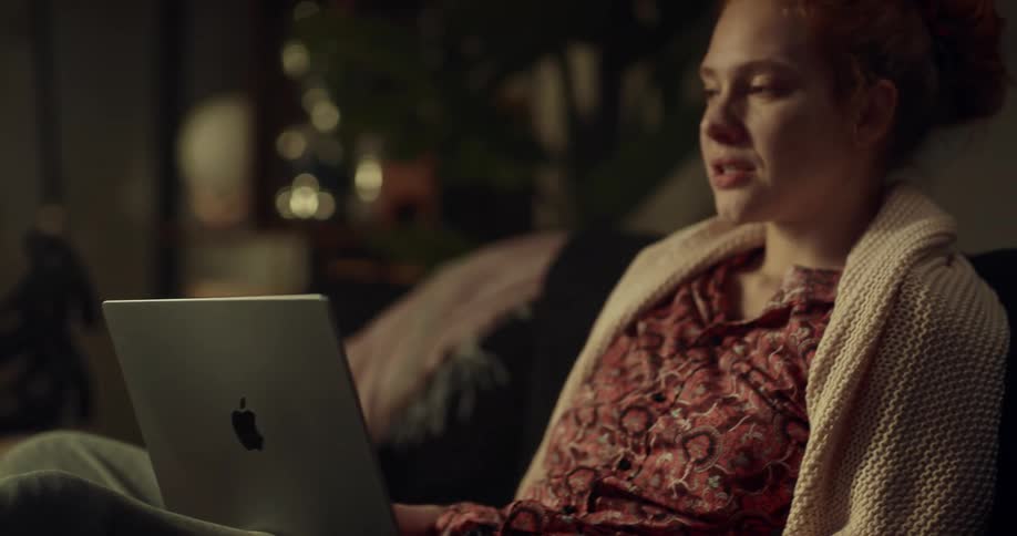 Woman with broken leg sits on couch making video call on laptop