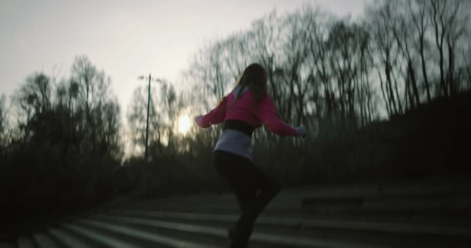 Woman runs forward up steps and backwards between flights of steps before dancing outdoors near leafless trees