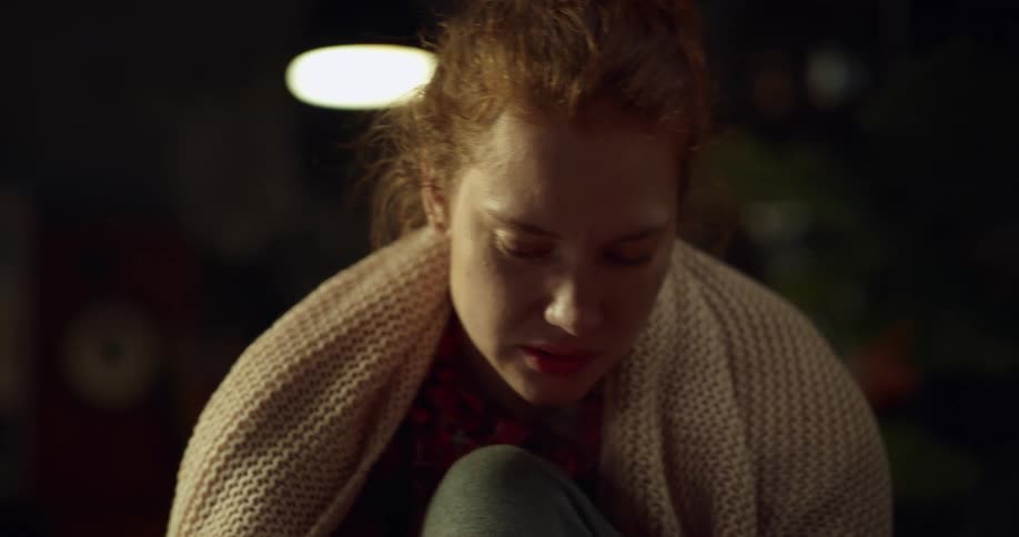 Young woman redhead sitting on couch at nighttime adjusting boot splint