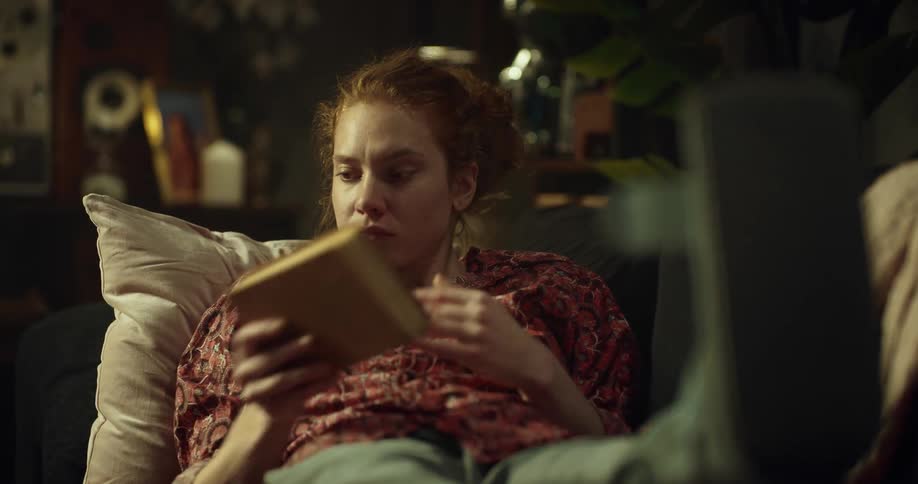 A woman is sitting on a couch and reading a book