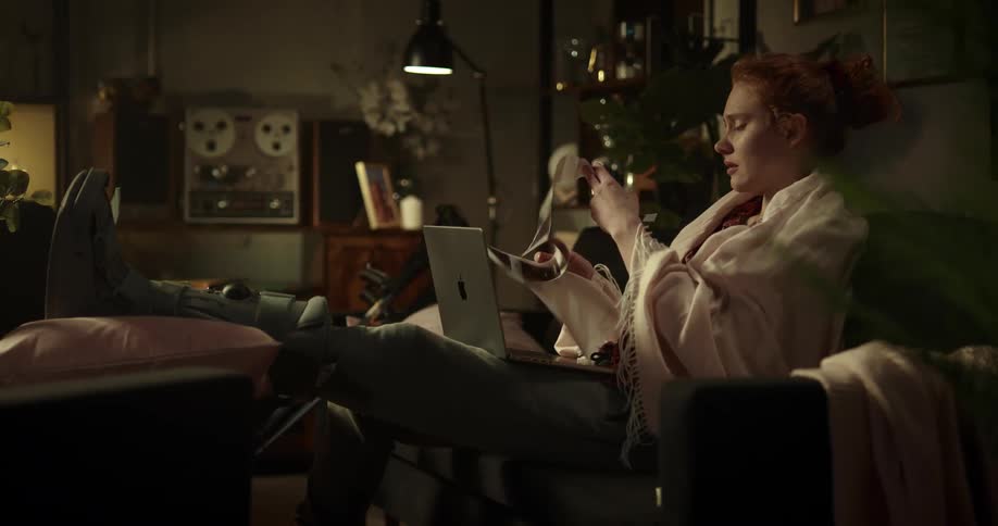 A woman is sitting indoors and looking at her laptop