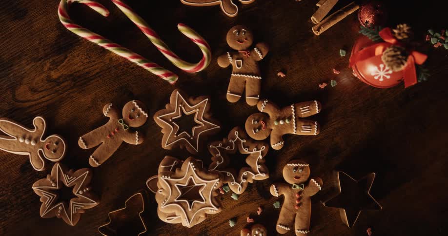 Holiday cookies are scattered on the table with candy canes as the smiling faces of gingerbread men are looking up