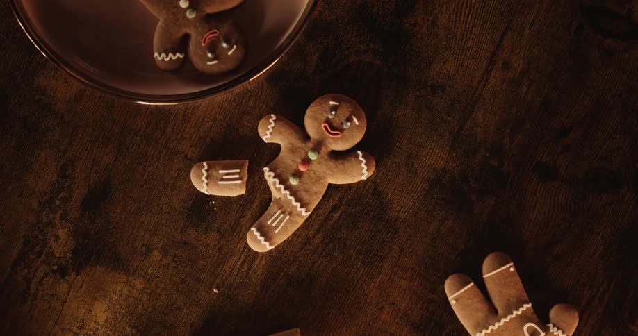 Two iced gingerbread men lie on table one with a broken leg while another gingerbread man lies in a bowl