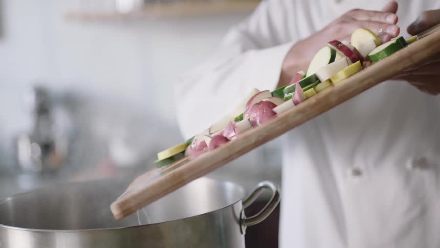 A person scrapes vegetables into a pot