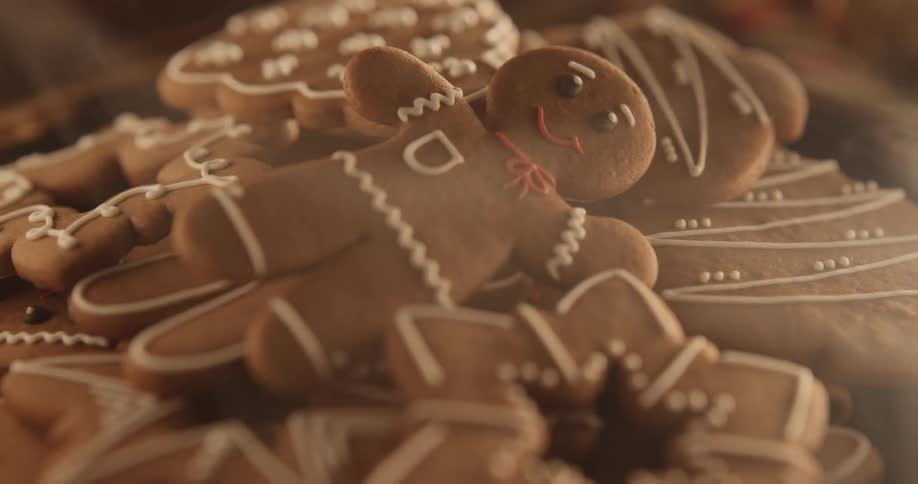 A smiling gingerbread man looks up from a plate of cookies as wisps of smoke move over the table