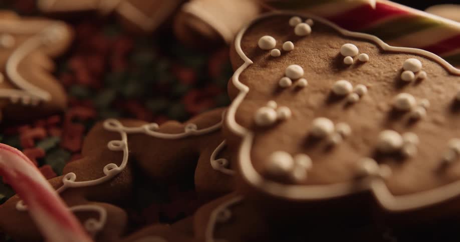 Holiday gingerbread cookies decorated with icing are on a table with a candy cane