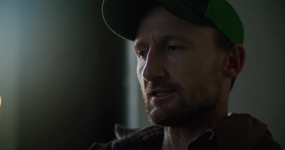 A man wearing a baseball cap is standing in a room speaking