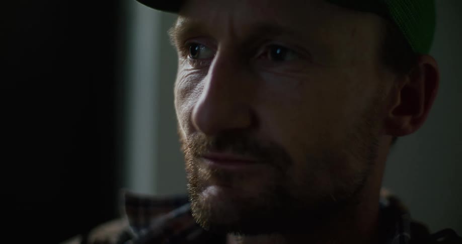 A man wearing a cap is speaking as light shines on his face