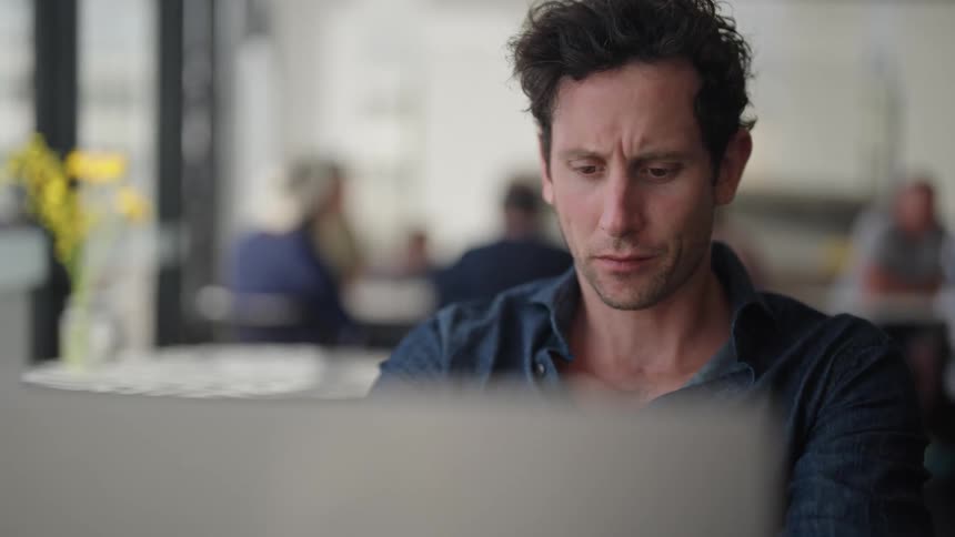 A white man is typing and looking intently at a computer screen while drinking a mug of coffee
