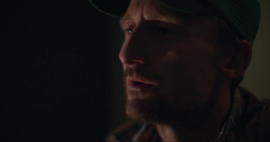A man is standing indoors by himself and wearing a hat
