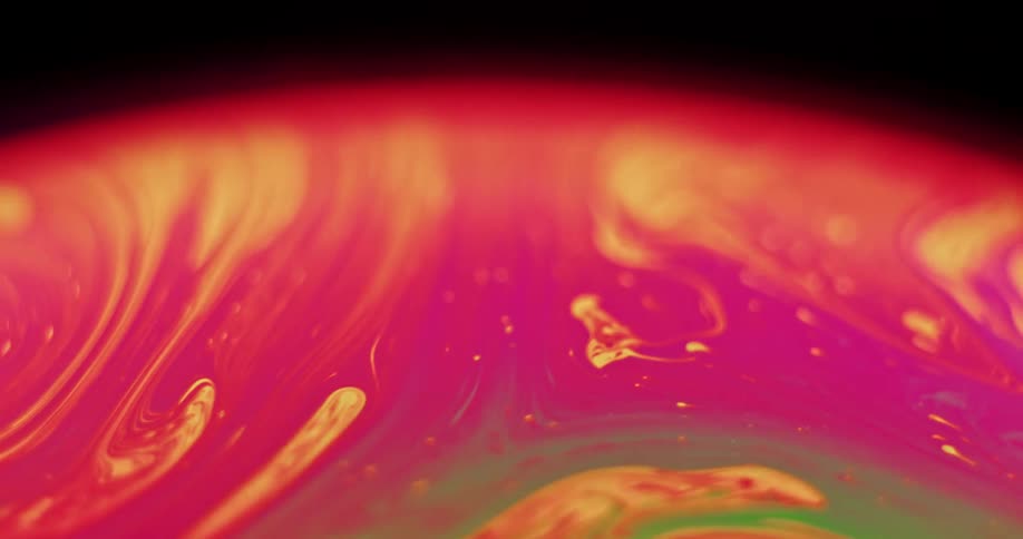 An orange and pink variegated substance moves over the surface of a glowing sphere with green wisps