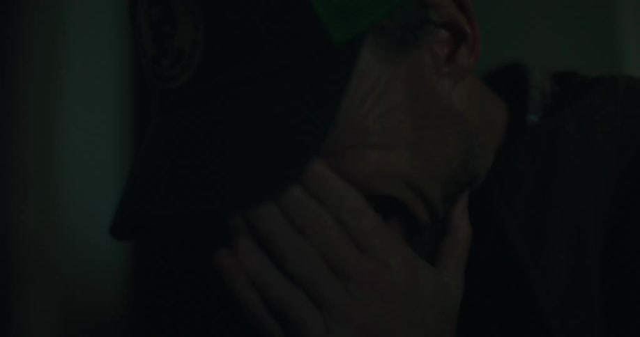 Man covers his face while crying in dark room lit by flashing blue and red lights