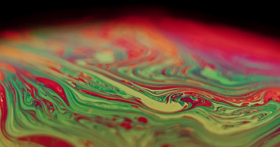 Green and red organic liquid is moving and mixing into variegated stripes as it moves over a sphere