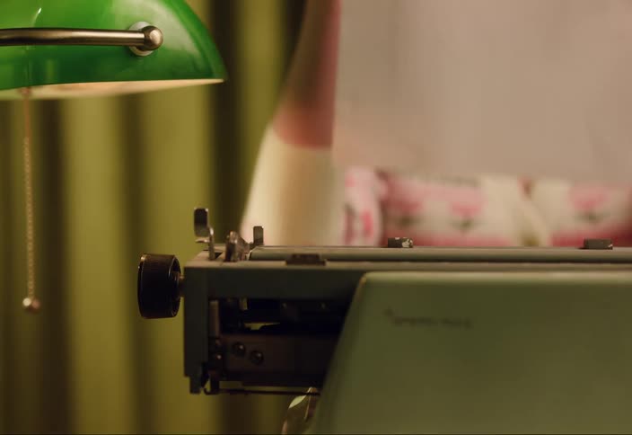 A woman is pulling a sheet of paper out of an old green typewriter